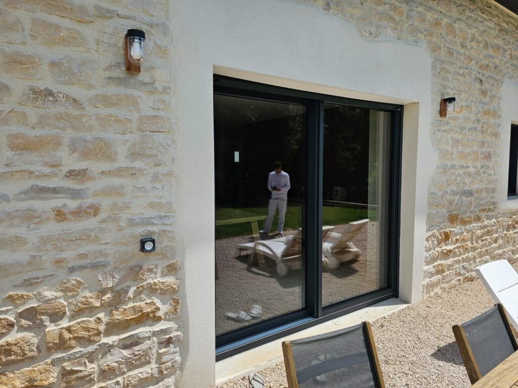 Baie vitrée coulissante Finstral gris anthracite 7016 sur mur en pierre avec accès terrasse à Échenon.