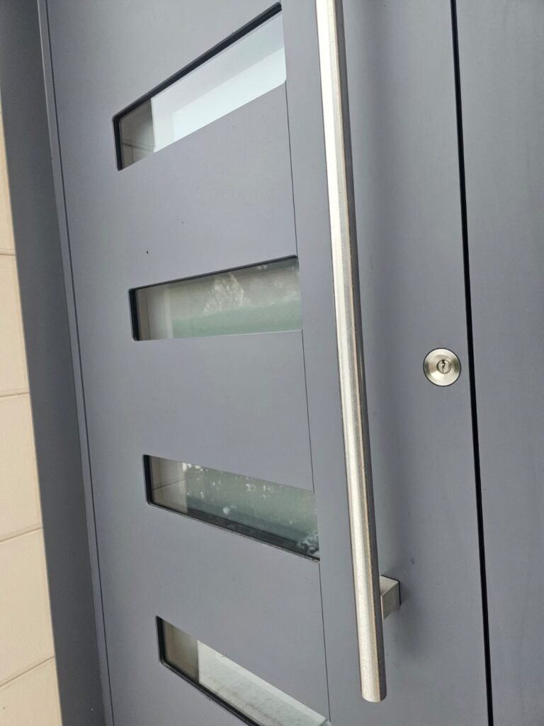 Gros plan porte d'entrée Inotherm gris anthracite avec barre de tirage inox et inserts vitrés Menuiserie Foultot Hortes Haute-Marne