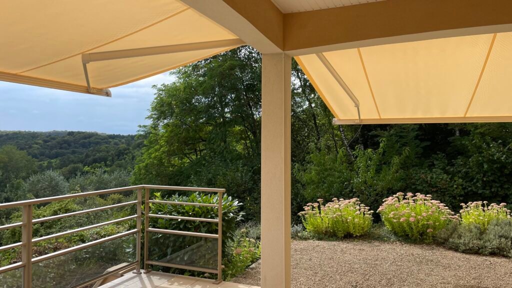 Vue depuis le dessous d'un double store banne de terrasse Brustor B25 beige déployé face à la nature à Euffigneix (52)