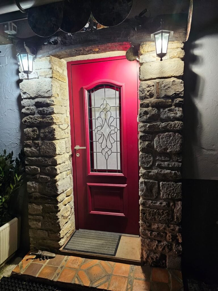 Porte d'entrée Inotherm rouge sous une voûte en pierre éclairée de nuit à Selongey