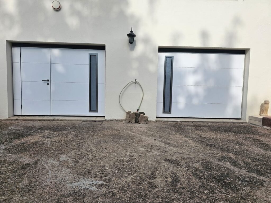 Vue d'ensemble de deux portes de garage Moos blanches avec insert vitré vertical côte à côte à Serqueux Haute-Marne, Menuiserie Foultot