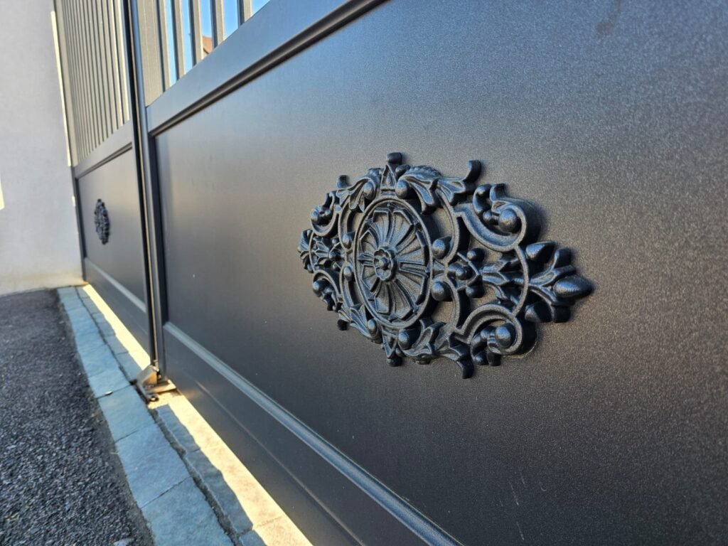 Gros plan sur une rosace décorative moulée en relief sur le soubassement d'un portail alu Cétal Pléiade.