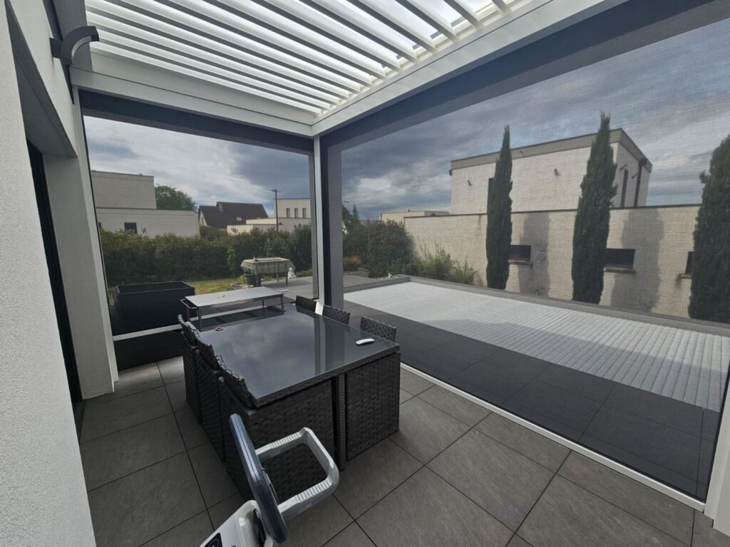 Terrasse couverte par une pergola bioclimatique avec screens latéraux fermés donnant sur un jardin