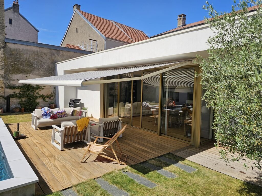 Store banne Brustor grande largeur déployé sur terrasse bois avec jardin et piscine Messigny-et-Vantoux Côte-d'Or, Menuiserie Foultot