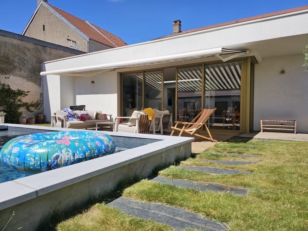 Store banne Brustor B50S au-dessus de la terrasse bois, piscine au premier plan, maison contemporaine à Messigny-et-Vantoux (21), Menuiserie Foultot