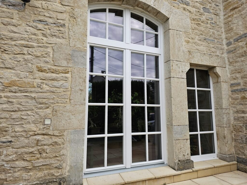 Façade maison en pierre avec fenêtre cintrée et fenêtre latérale Finstral PVC imitation bois Menuiserie Foultot Côte-d'Or