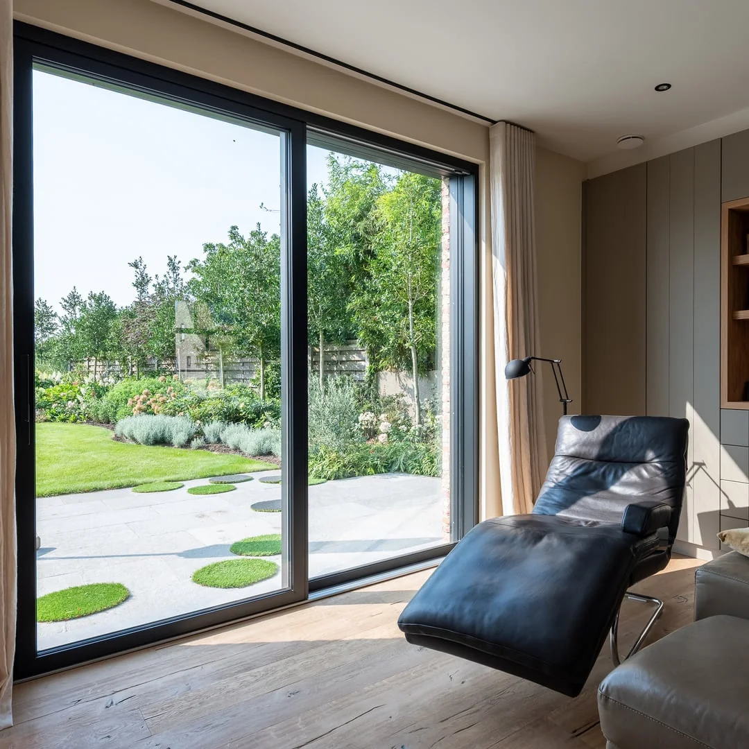 Baie vitrée levant-coulissant Finstral, cadre aluminium noir, ouverte sur une terrasse et un jardin depuis un salon (photo Finstral)