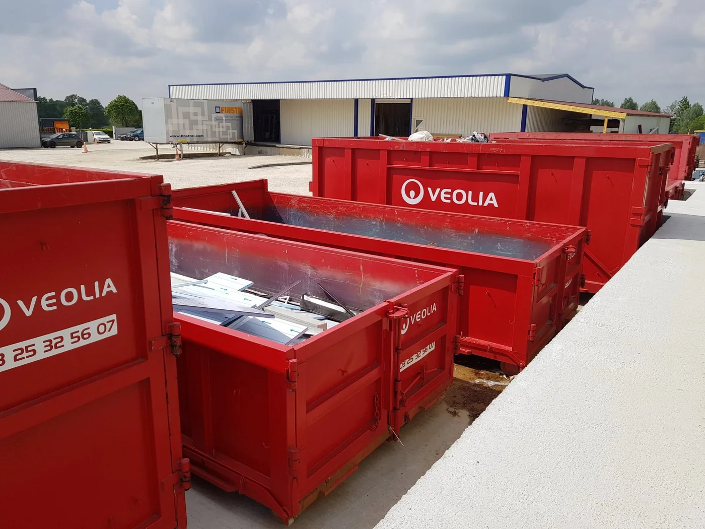 Bennes de tri Veolia alignées sur le dépôt de Menuiserie Foultot à Chalindrey, chargées de vitrages et d'anciennes menuiseries déposées en chantier, devant un camion de livraison Finstral
