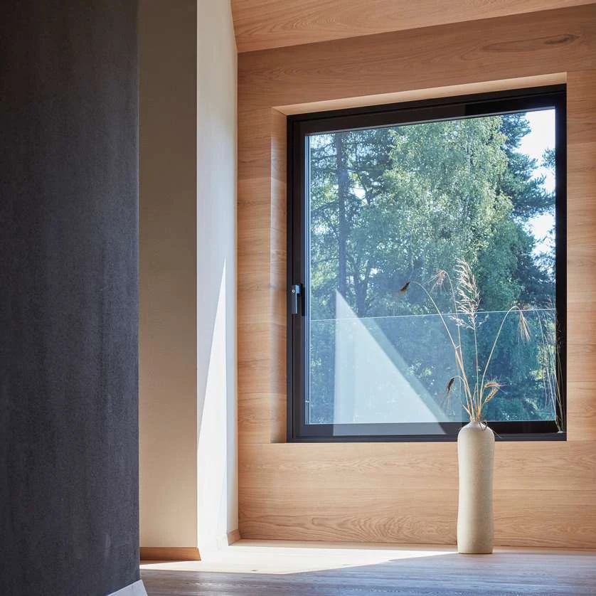 Fenêtre aluminium Finstral noire avec ouvrant Cristal tout en verre côté intérieur, dans une embrasure habillée de bois clair (photo Finstral)