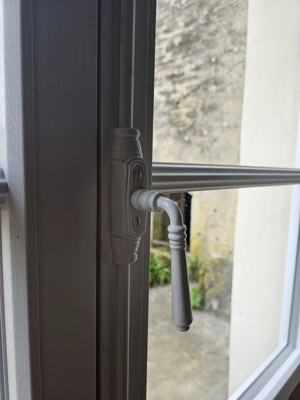 Fenêtre PVC Finstral blanche à surface structurée, petite moulure et poignée de style ancien, posée par Menuiserie Foultot dans une maison en pierre