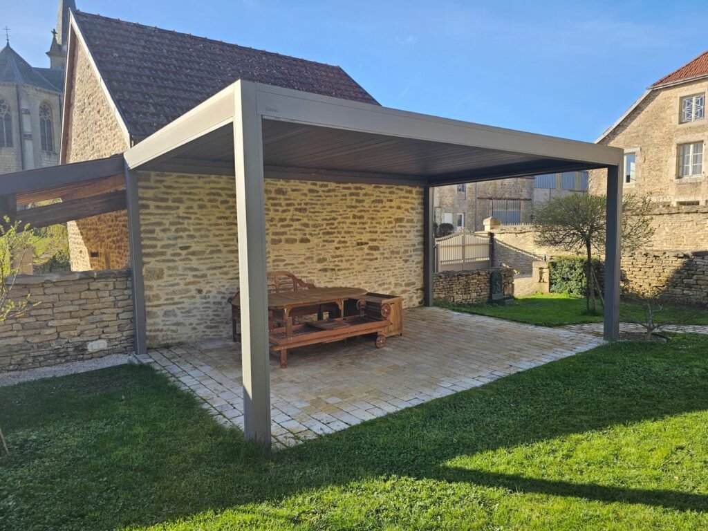 Pergola bioclimatique Brustor B200XL RAL 7039 posée dans une cour en pierres apparentes à Bourg (52) – Menuiserie Foultot