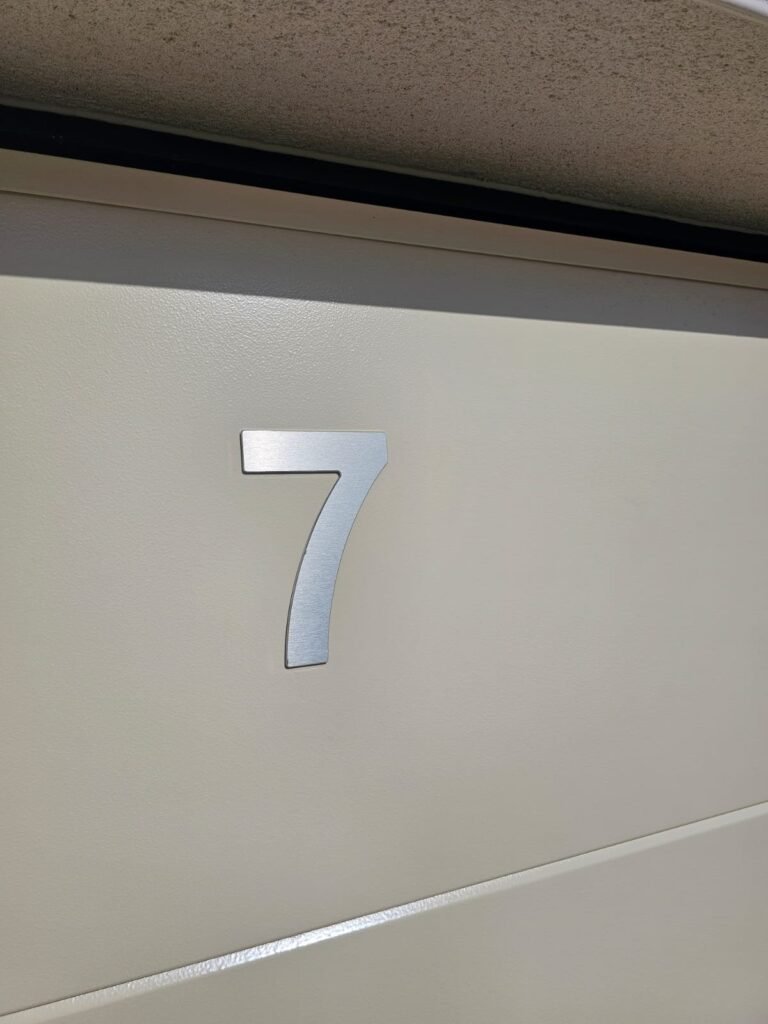 Gros plan numéro de maison 7 en aluminium sur porte de garage Moos - Varois-et-Chaignot, Menuiserie Foultot