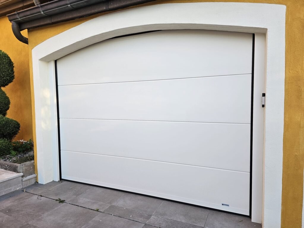 Porte de garage sectionnelle Gypass blanc cassé sous un arc cintré en enduit blanc, Rouvres-en-Plaine