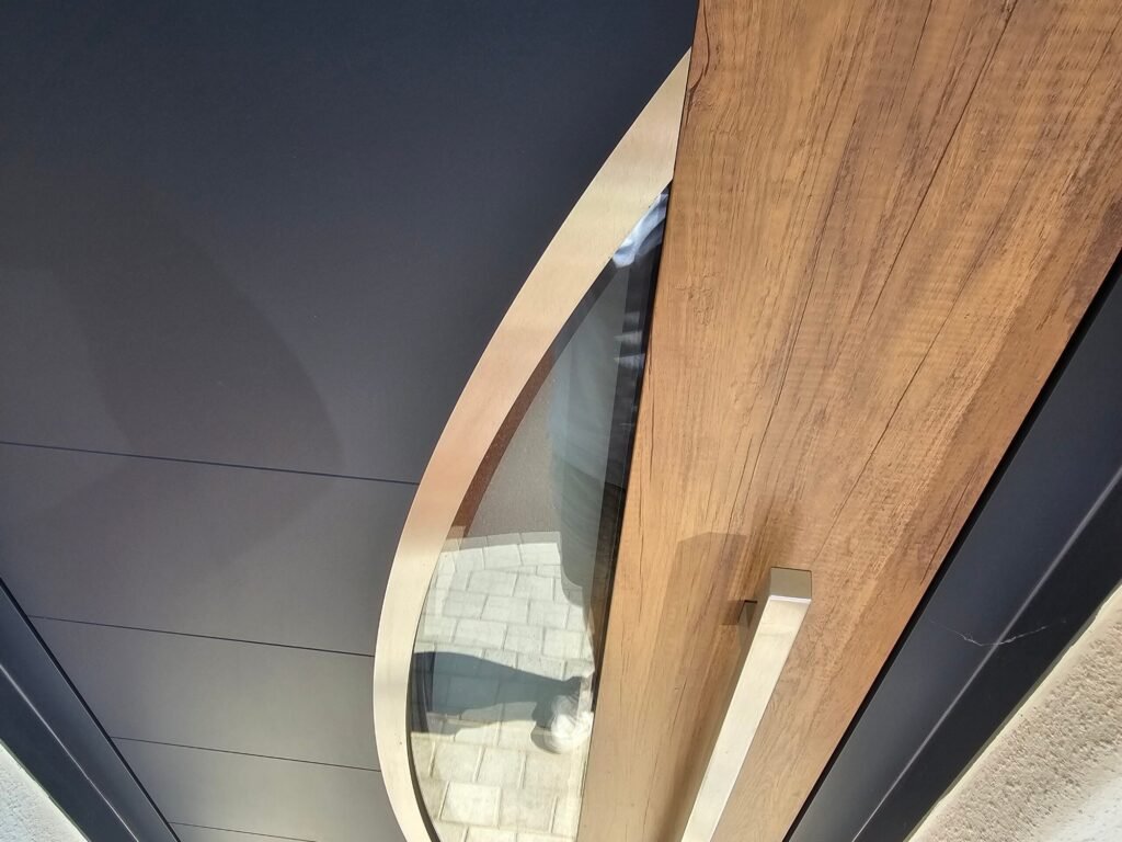 Gros plan en plongée sur la jonction insert ovale inox, montant aspect chêne et panneau anthracite de la porte Inotherm - Chenôve, Menuiserie Foultot