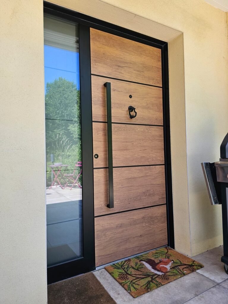 Vue de biais de la porte Inotherm de Langres : barre de tirage noire, filets noirs sur le décor chêne vieilli et filigranes alignés dans le fixe vitré