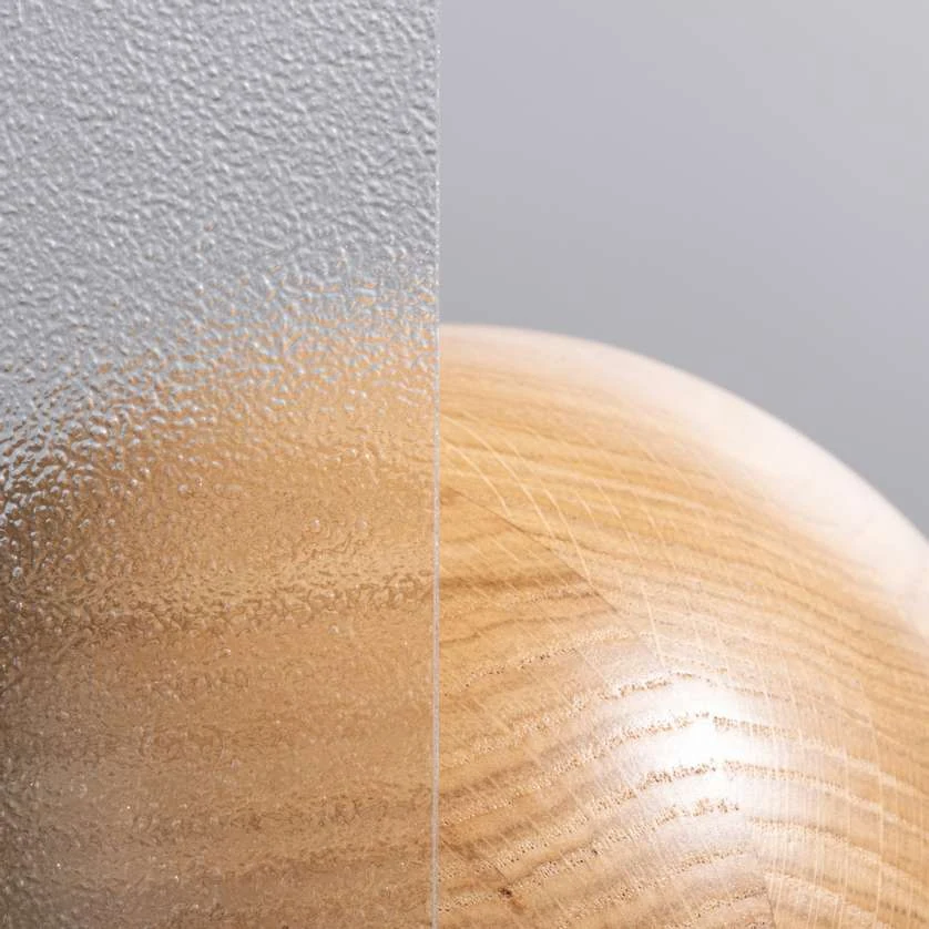 Sphère en bois vue à travers un verre ornemental granité à gauche et un verre clair à droite : la forme et la lumière passent, le détail non (photo Finstral)