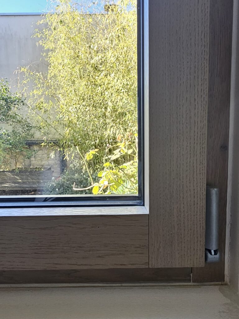 Détail de l’angle du cadre en bois d’une fenêtre Finstral alu-bois, avec le veinage du bois et la paumelle