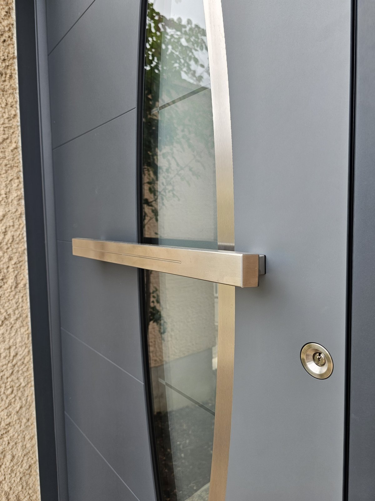 Vitrage en fuseau intégré au panneau d'une porte d'entrée aluminium Inotherm grise, traversé par une poignée barre inox