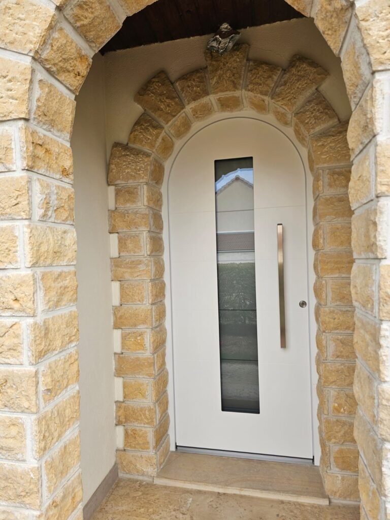 Porte d'entrée cintrée en aluminium blanc Inotherm RAL 9016 posée dans un arc de pierre à Orgeux par Menuiserie Foultot