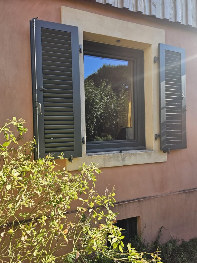 Fenêtre Finstral gris RAL 7022 encadrée de volets battants aluminium Ehret à lames orientables ouverts, à Dijon
